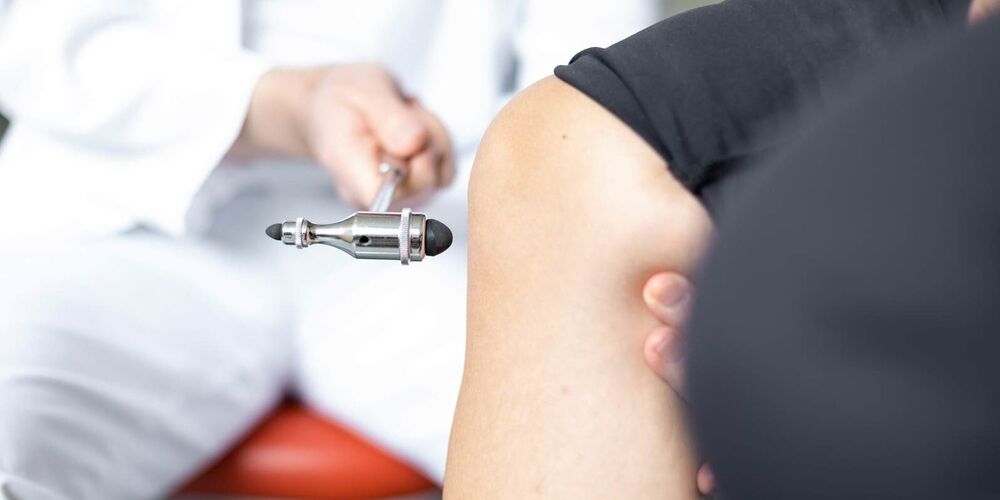 Ein Arzt klopft mit einem kleinen Hammer gegen das Knie eines Patienten. 
