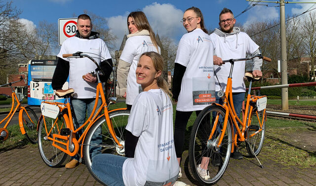 Einige junge Menschen tragen Augustinus Tshirts und haben zwei Fahrräder bei sich. Eine junge Frau kniet vor den anderen vier. 