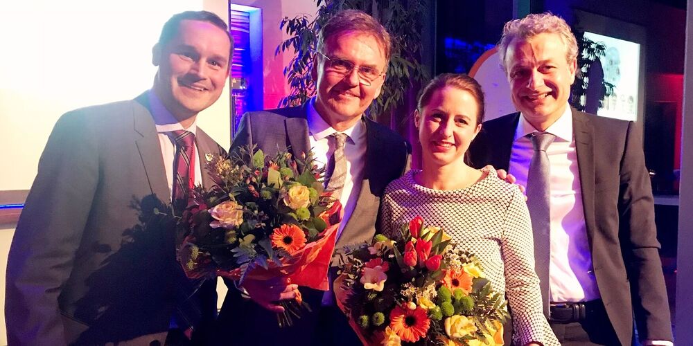 Drei Männer und eine Frau bei einer Preisverleihung. Die Frau und ein Mann haben einen Blumenstrauß in der Hand und alle vier gucken lächelnd in die Kamera.
