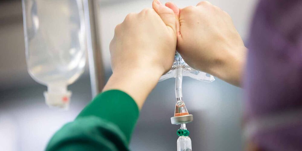 Zwei Hände drücken einen Infusionsbeutel.
