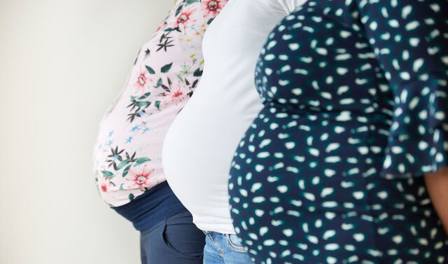 Drei schwangere Frauen zeigen hintereinander stehend ihren Babybauch in die Kamera