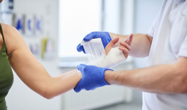 Mitarbeiter legt einer Patientin einen Verband um das Handgelenk. 