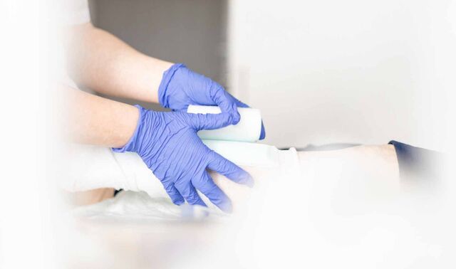 Eine Person, welche Hygienehandschuhe trägt legt einer anderen Person einen Verband an. 