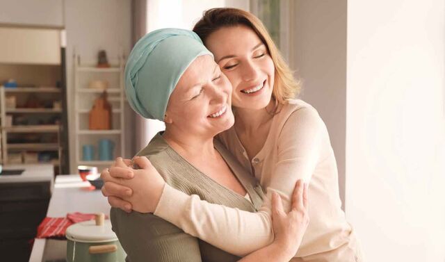 Eine Krebspatientin mit Kopftuch wird von einer anderen Frau umarmt. Beide lächeln. 