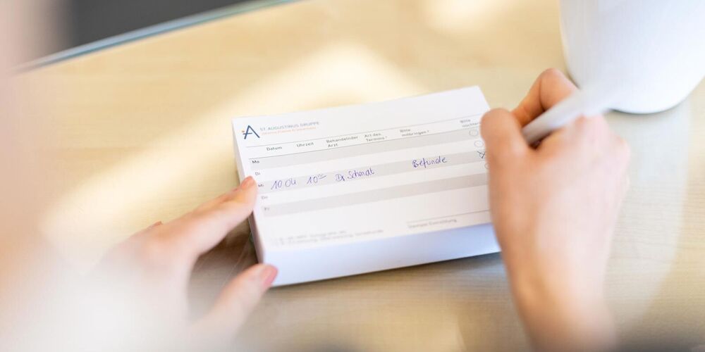 Eine Person schreibt etwas auf einen Terminzettel. 
