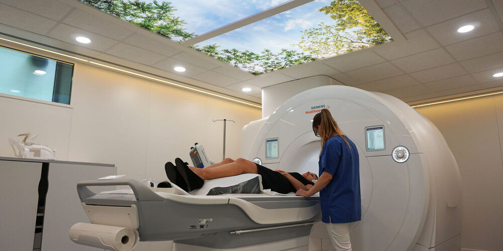 Eine Patientin wird in ein MRT-Gerät zur Untersuchung gefahren. Hierbei steht ihr eine Krankenpflegerin zur Seite.