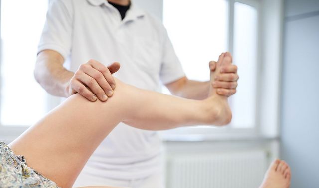 Physiotherapeut hält das Bein eine Patientin an Fuß und Knie fest und hilft dieser bei den Übungen.
